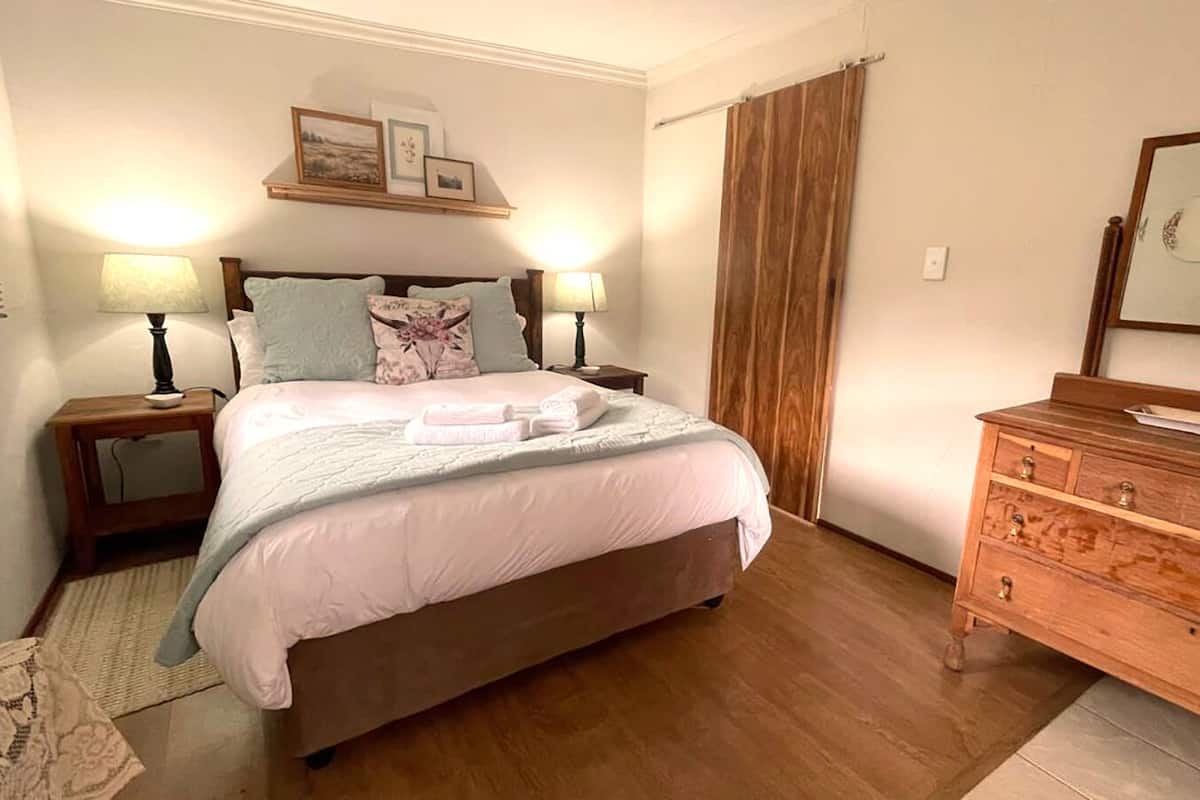 A bedroom with a large bed, two bedside tables with lamps, a wooden dresser, and a wooden headboard.