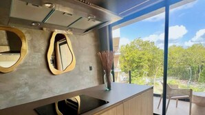 A modern kitchen with a large island, two wall-mounted mirrors, and a view of the outdoors through large glass doors.