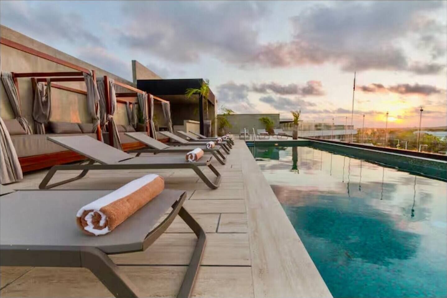 A rooftop pool area with lounge chairs and a view of the sunset.