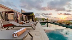 A rooftop pool area with lounge chairs and a view of the sunset.