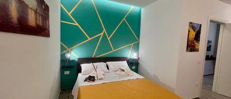 A modern hotel room with a geometric-patterned headboard, a neatly made bed, and a bright yellow throw blanket.