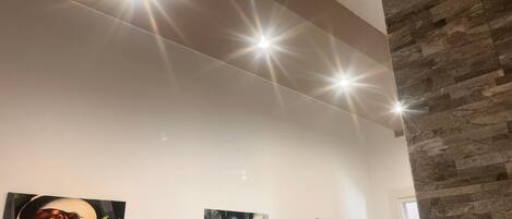 A room with a stone accent wall, three paintings on the wall, and recessed ceiling lighting.