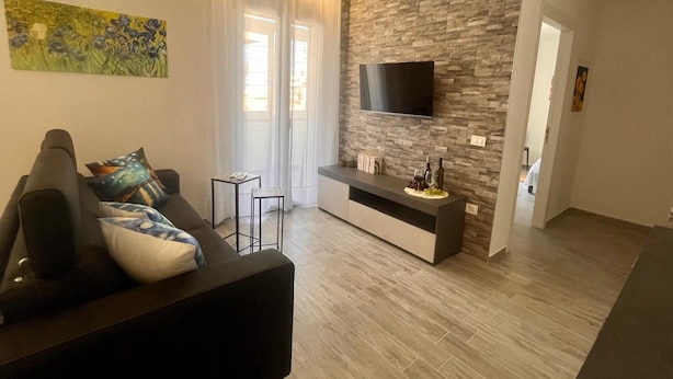 Una sala de estar moderna con un sofá negro, un televisor de pantalla plana montado en una pared de piedra y una pequeña mesa con adornos.