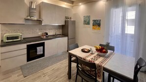 Una cocina moderna con comedor, que incluye un horno empotrado, un refrigerador y un lavamanos. Hay dos sillas y una mesa con un frutero y un plato de comida.
