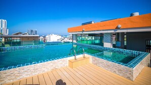 A rooftop infinity pool with a wooden deck and a stone wall, overlooking a cityscape. - Phuket Patong Buri Resort (Patong)