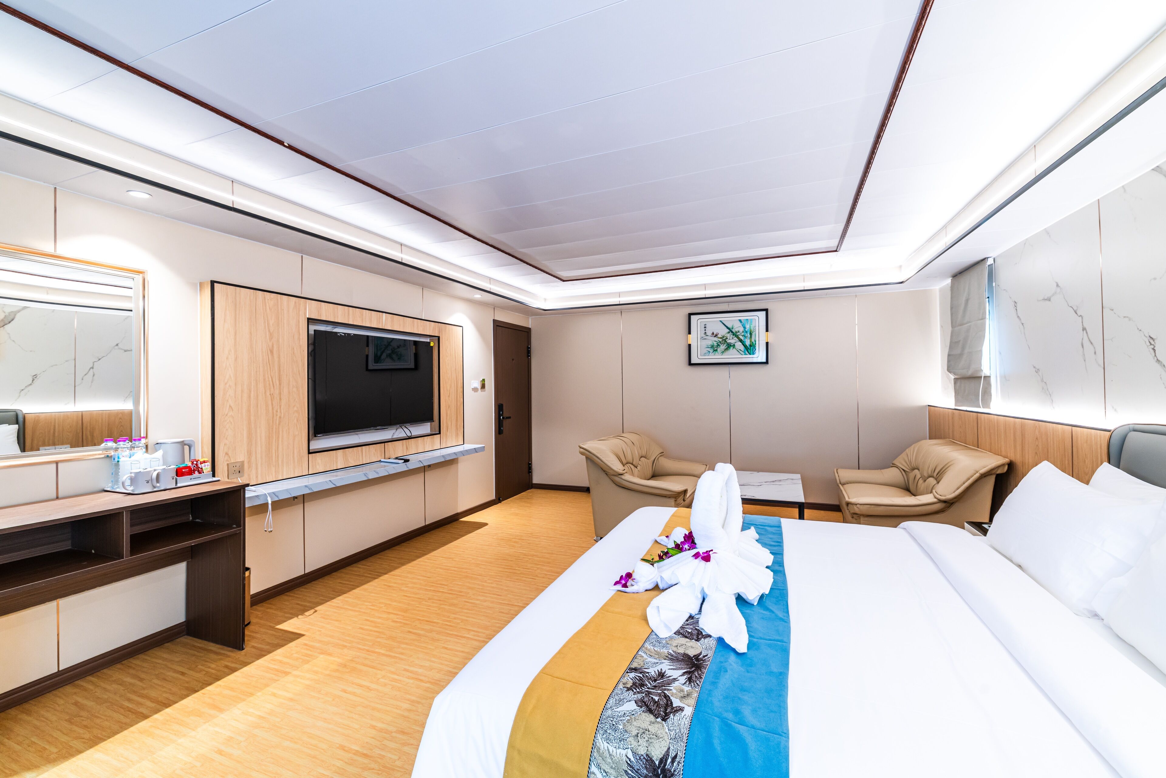 A modern hotel room with a large bed, a desk, a TV, and a seating area.