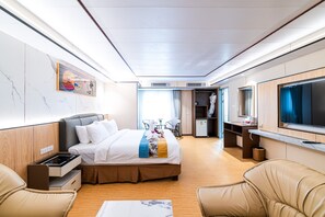 Moderni hotellihuone, jossa on sänky, oleskelualue ja televisio.