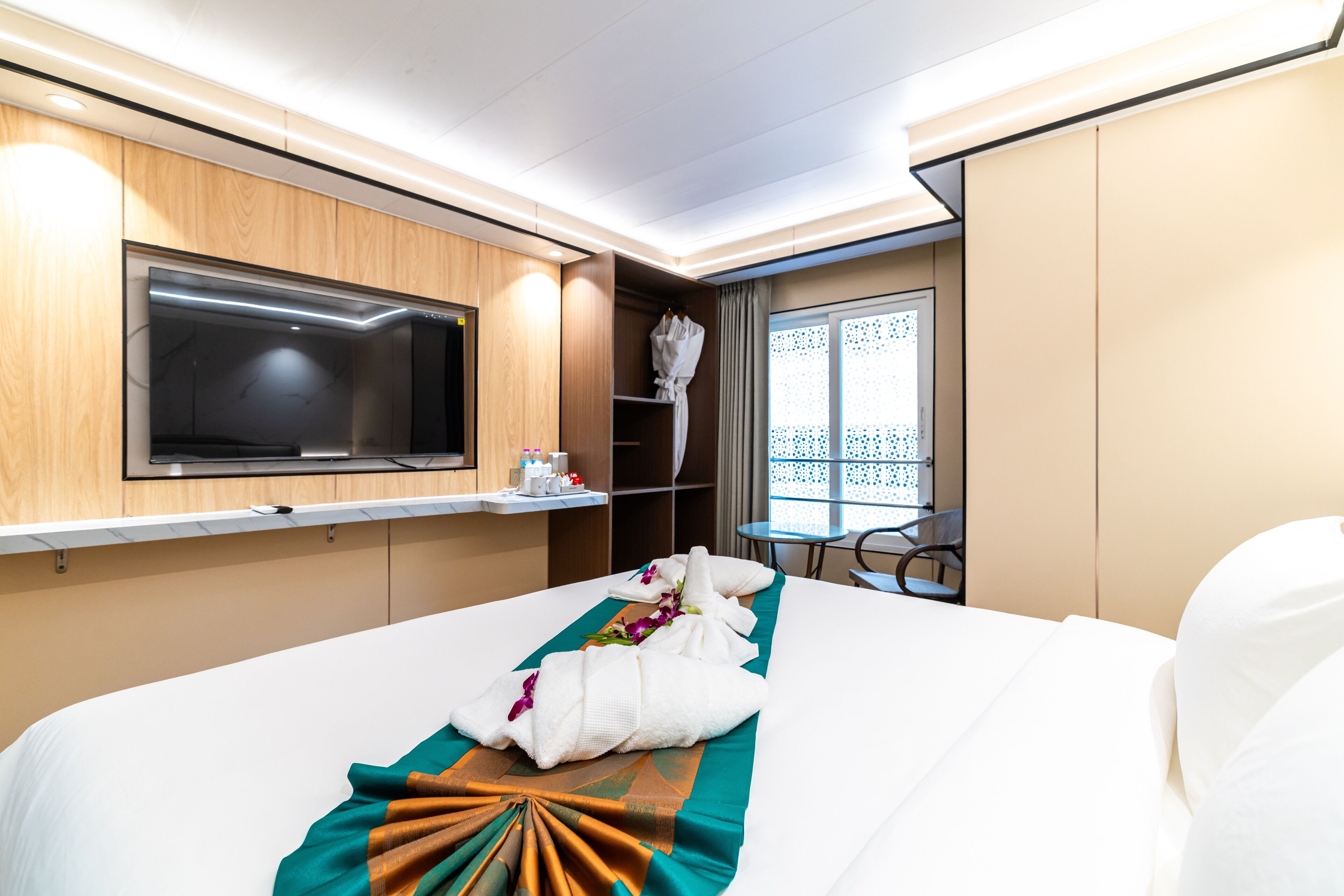 A hotel room with a large bed, a TV mounted on the wall, a small table, and a window with a view of the outside.