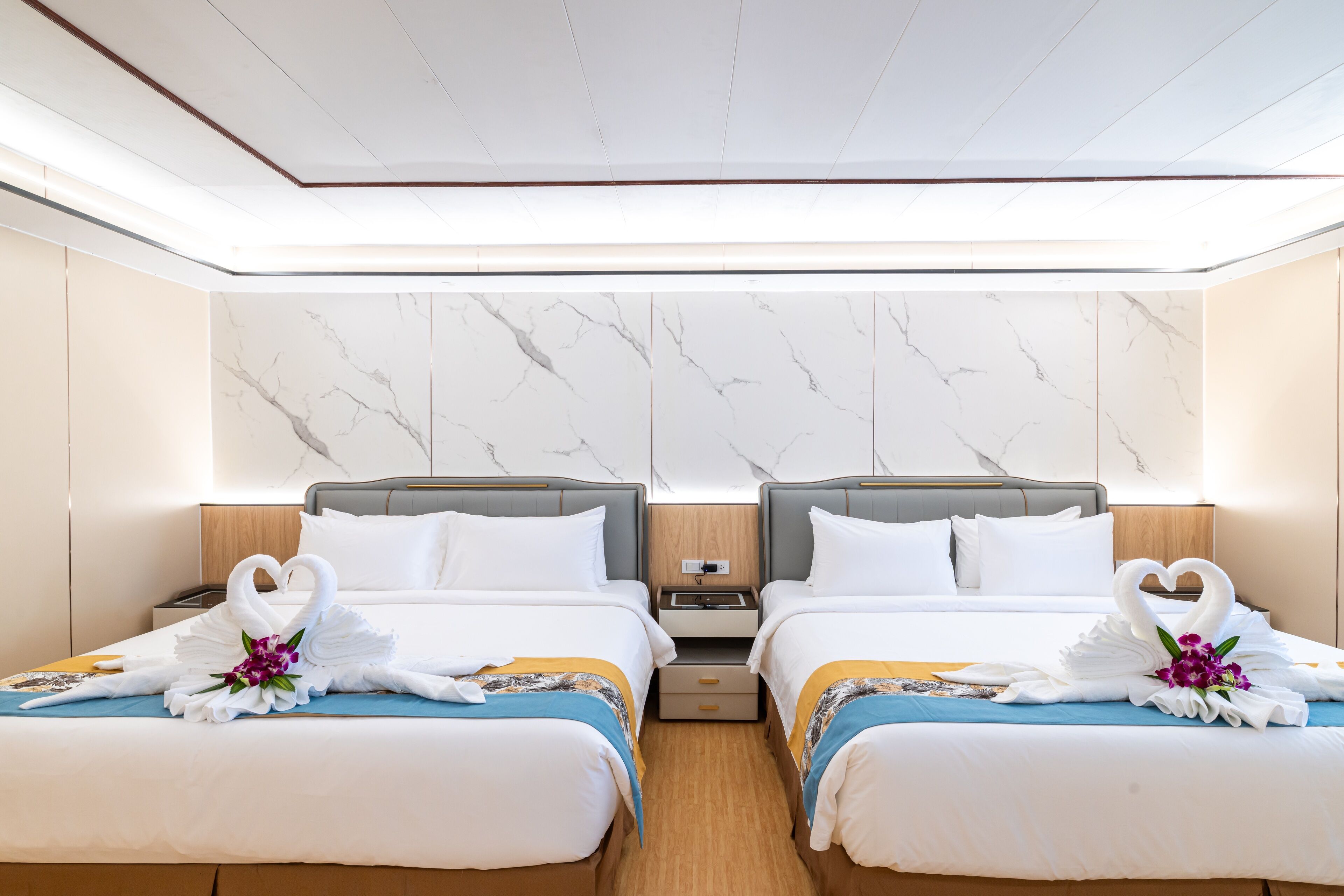 A hotel room with two beds, marble-patterned walls, and decorative swan-shaped towels.