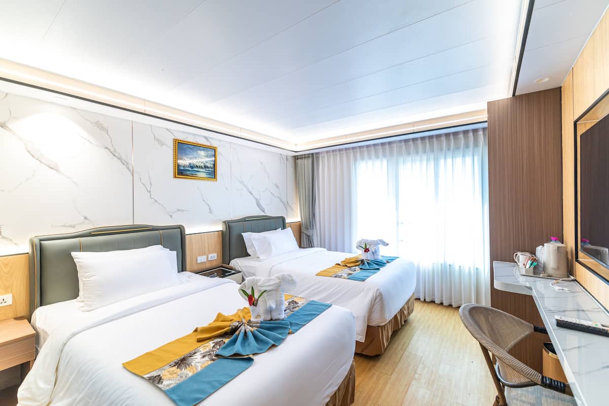 Une chambre d’hôtel avec deux lits, un bureau, une chaise, une télévision et une fenêtre avec des rideaux.