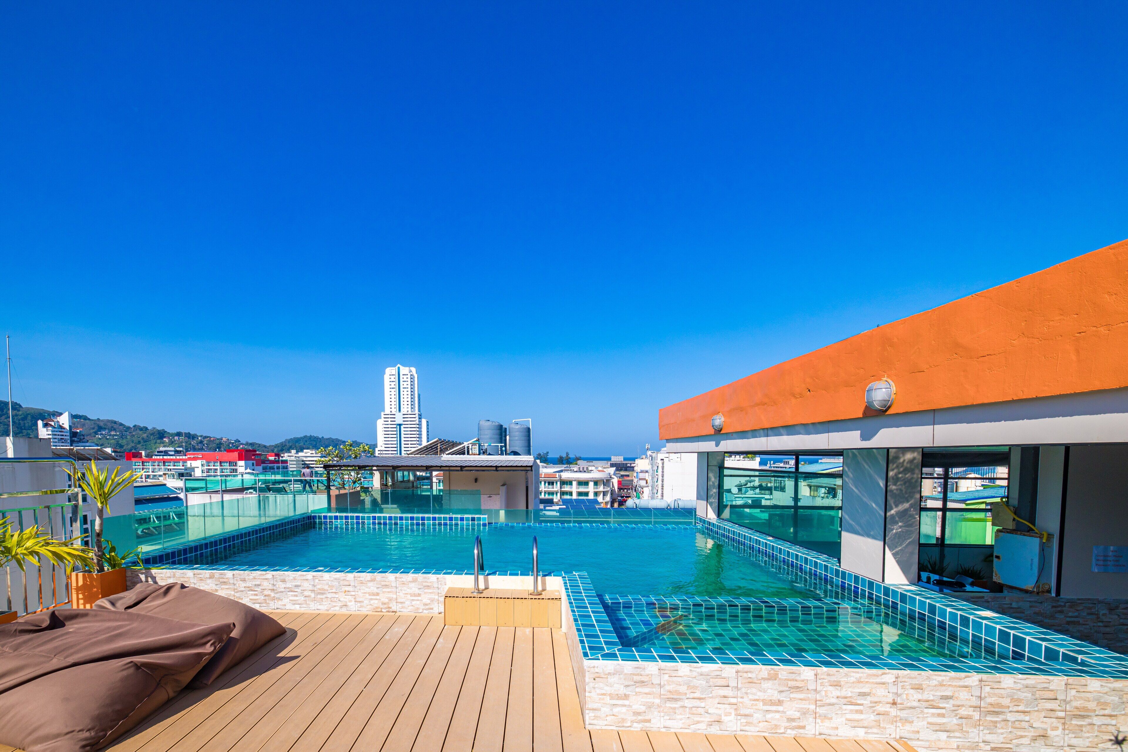 A rooftop pool with clear blue water, a wooden deck, and a view of the city skyline.