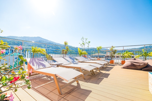 A rooftop lounge with sun loungers and potted plants.