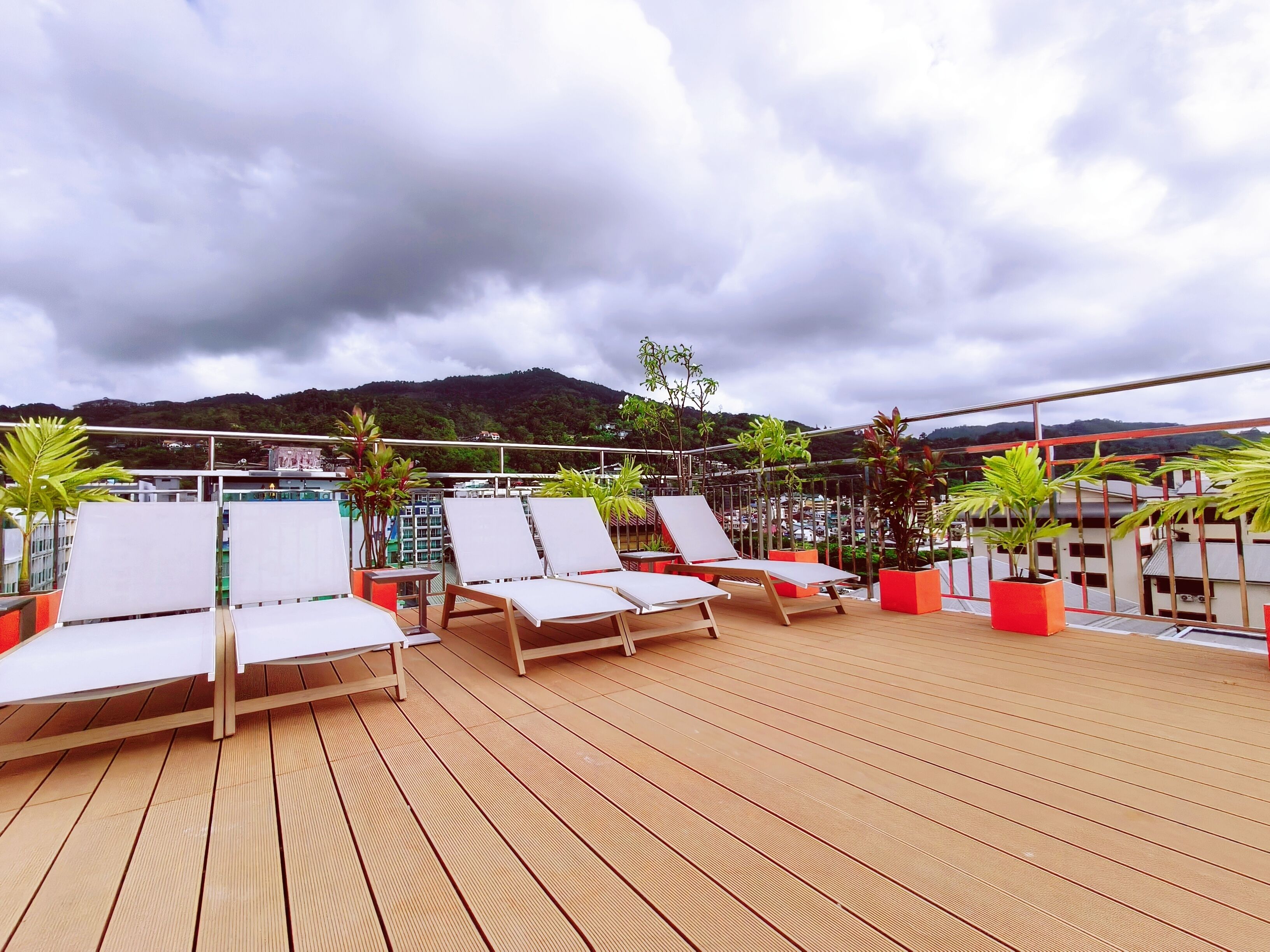 A rooftop deck with white lounge chairs and potted plants.