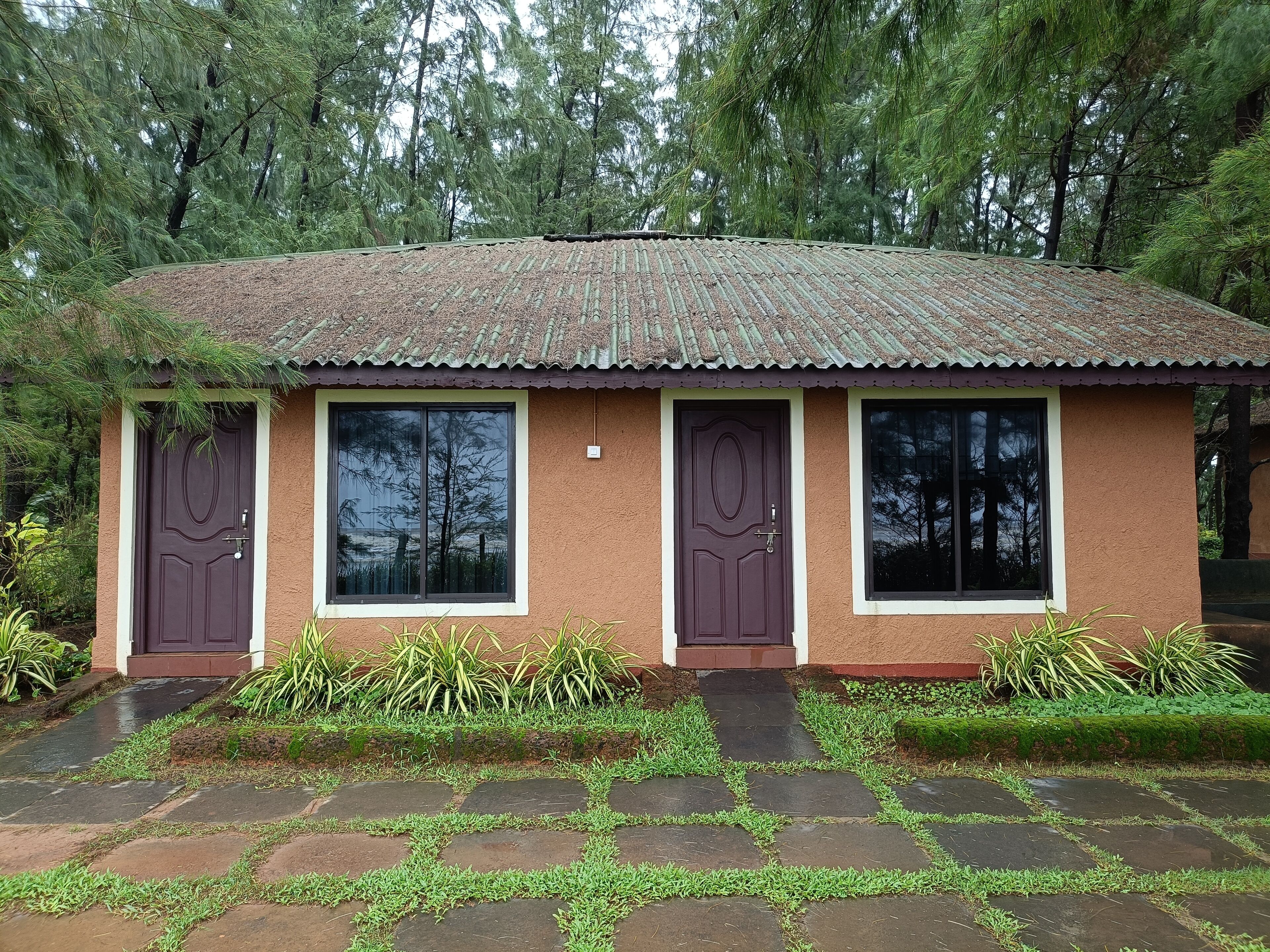 Um pequeno edifício térreo com telhado de cerâmica, três janelas e uma porta. Está rodeado por vegetação e possui um caminho de pedra que leva à entrada.