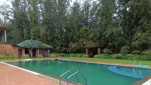 Una piscina con solárium empedrado, una zona de estar cubierta pequeña y abundante vegetación al fondo.
