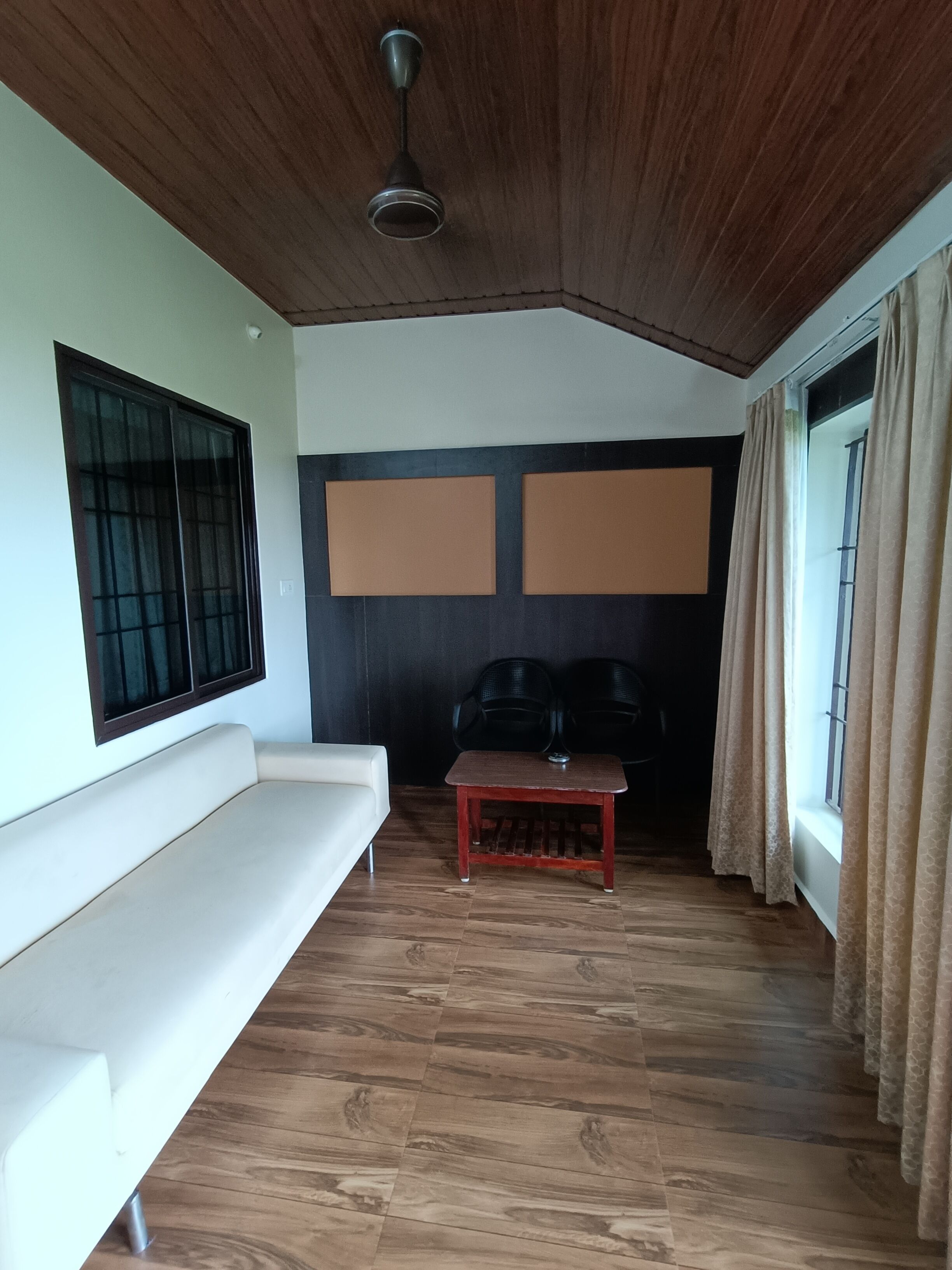 Una habitación con techo de madera, un sofá blanco, una pequeña mesa de madera y una ventana con cortinas.