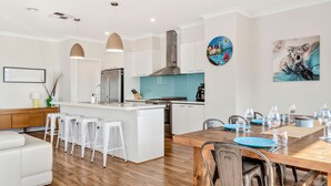 Una cocina moderna con armarios blancos, una isla central y un comedor con mesa y sillas de madera.