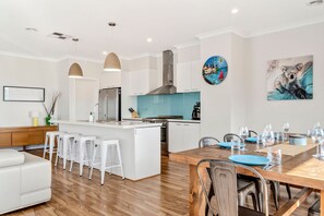 Una cocina moderna con armarios blancos, una isla central y un comedor con mesa y sillas de madera.