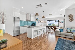 A modern kitchen with a central island, bar stools, a dining area with a table and chairs, and a living room with a sofa and a rug. - Beach Gum (Apollo Bay)