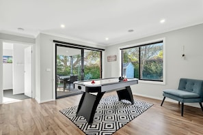 Una sala de estar moderna con mesa de fútbol, un sofá azul y ventanas amplias con vistas al exterior.