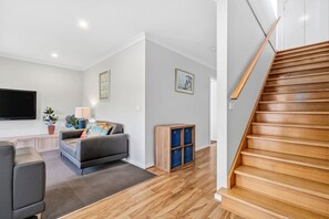 A modern living room with a grey sofa, a flat-screen TV, and a wooden staircase. - Beach Gum (Apollo Bay)