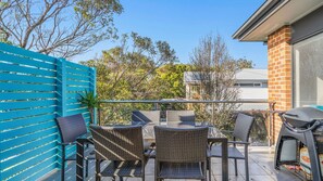 A balcony with wicker furniture, a barbecue grill, and a blue fence. - Beach Gum - A Stylish Coastal Retreat (Apollo Bay)