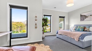 Un dormitorio moderno con ventanas amplias, una cama con muchas almohadas y vistas a zonas verdes.