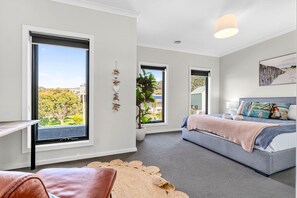 Un dormitorio moderno con ventanas amplias, una cama con muchas almohadas y vistas a zonas verdes.