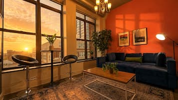 A modern living room with a large window, a blue sofa, a coffee table, and a chandelier.