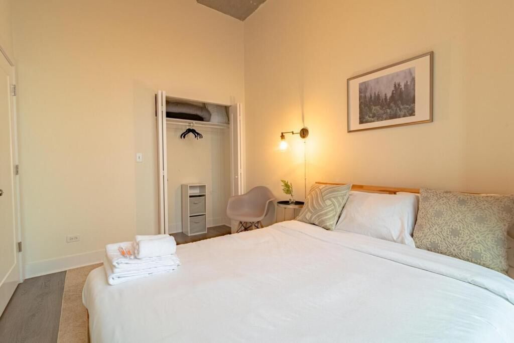 A hotel room with a bed, a chair, a desk, a wardrobe, and a painting on the wall.