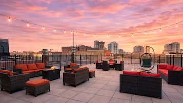 A rooftop terrace with outdoor seating, string lights, and a city skyline view.