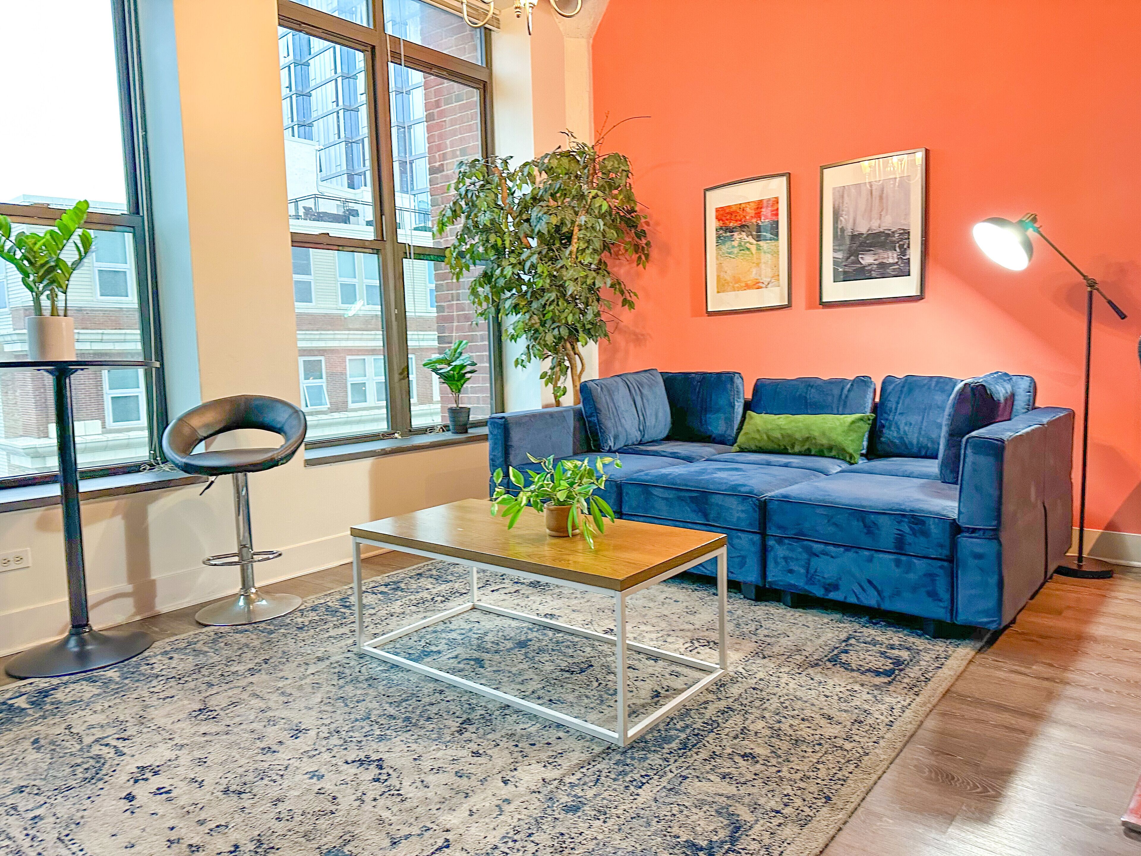 A modern living room with a blue sofa, a wooden coffee table, a potted plant, and a large window.