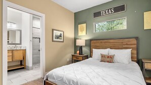 Un dormitorio con cama, mesita de noche, espejo, puerta y pared con un cartel que dice 'TEXAS'.