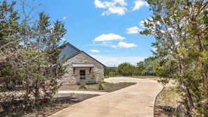 Una casa de piedra con un camino curvo, rodeada de árboles y arbustos.