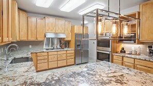 Una cocina moderna con armarios de madera, un refrigerador de acero inoxidable, horno empotrado y encimera de mármol.