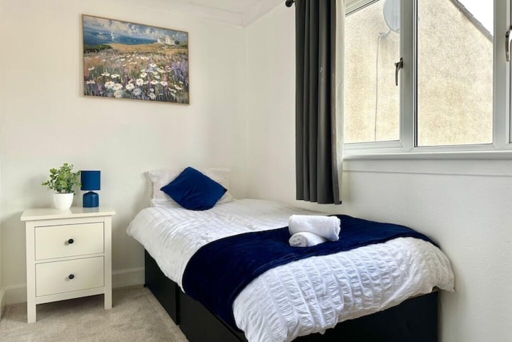 Une chambre à coucher avec un lit, une table de chevet, un tableau et une fenêtre.