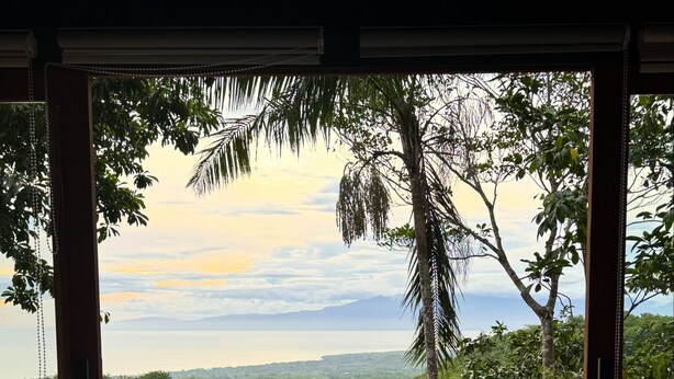 A woman sitting by a pool with a view of lush greenery and a body of water. - DRAKO VILLAS (San Juan)