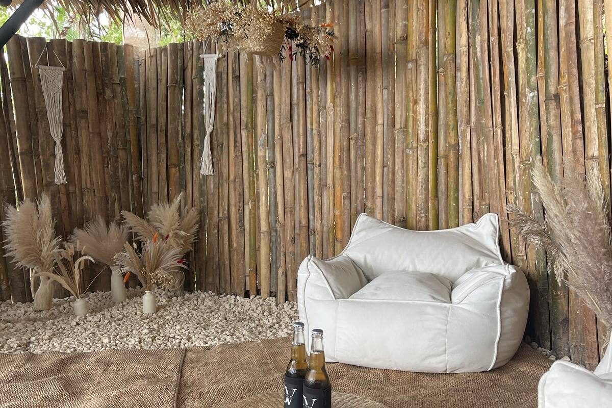 A rustic room with a bamboo wall, a white cushioned seating area, and decorative plants.