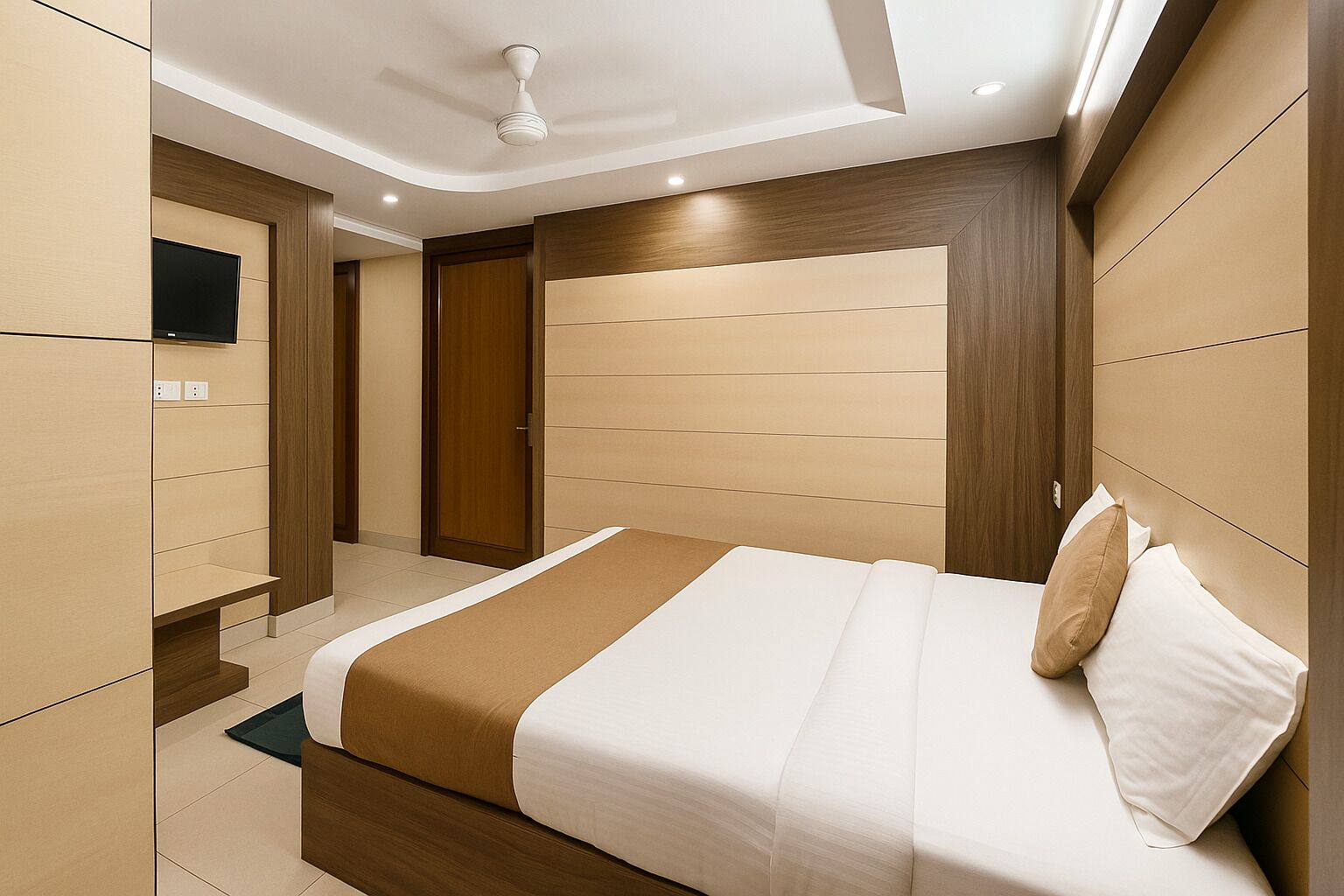 A modern hotel room with a large bed, wooden headboard, and a flat-screen TV mounted on the wall.