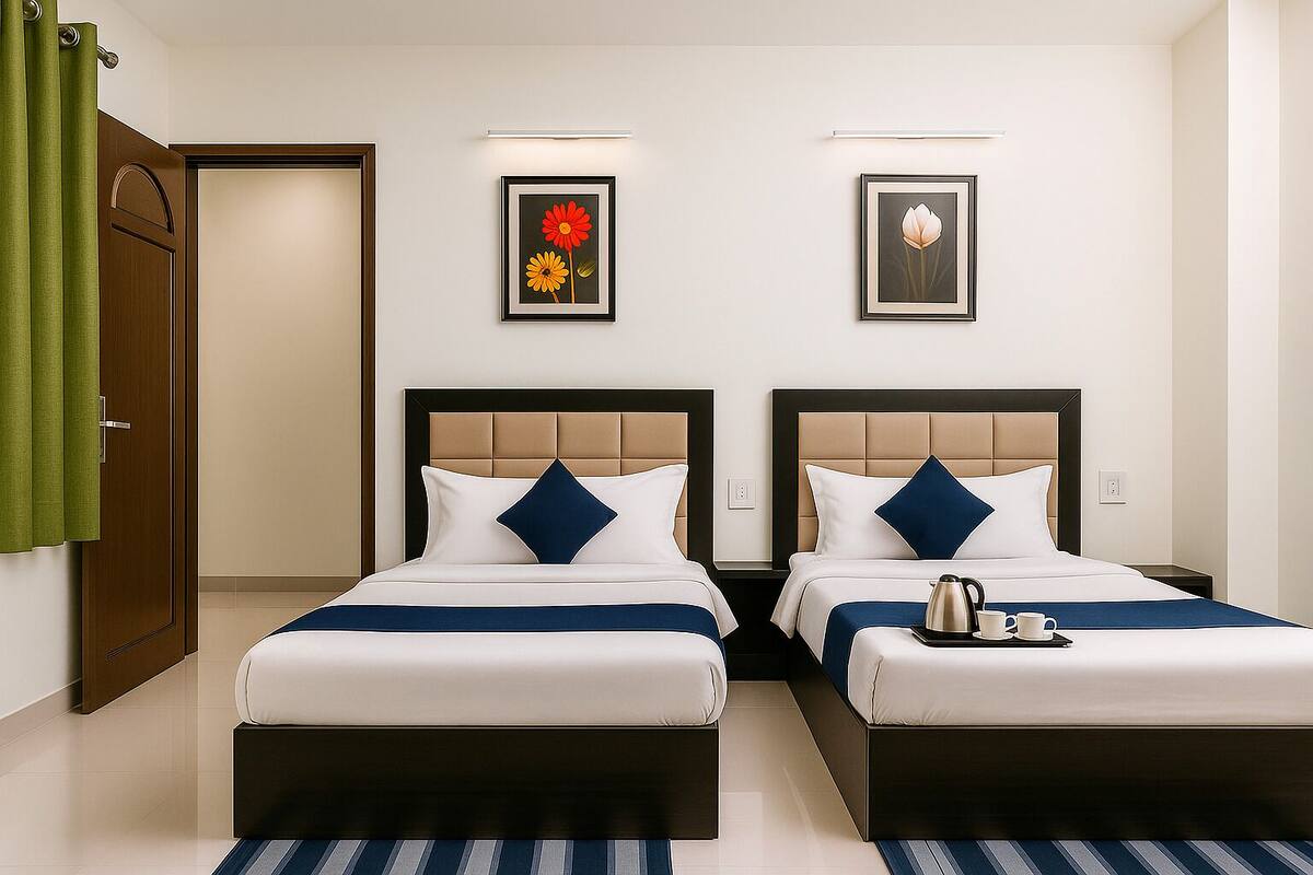 A hotel room with two beds, a green door, and two framed floral artworks on the wall.