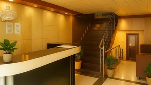 A reception area with a counter, potted plants, a staircase, and a door. - Hotel Lajja Palace (Haridwar)