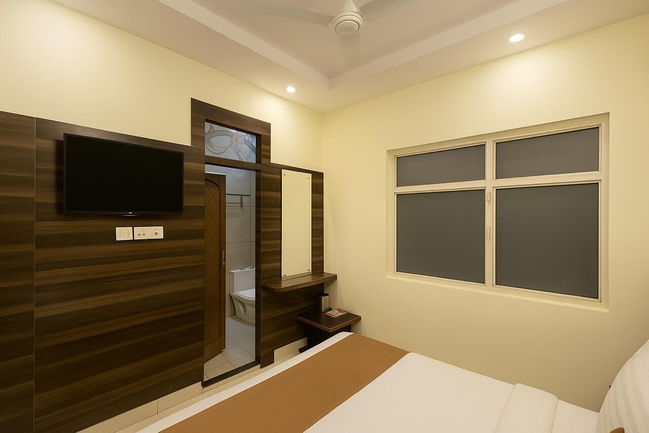 A hotel room with a bed, a TV mounted on the wall, a window, and a door leading to a bathroom.