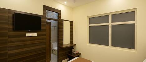 A hotel room with a bed, a TV mounted on the wall, a window, and a door leading to a bathroom.