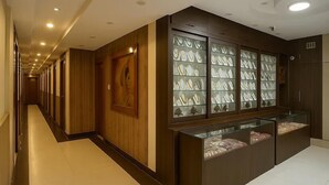 A hotel corridor with wooden paneling, a glass display case with jewelry, and a reception area. - Hotel Lajja Palace (Haridwar)