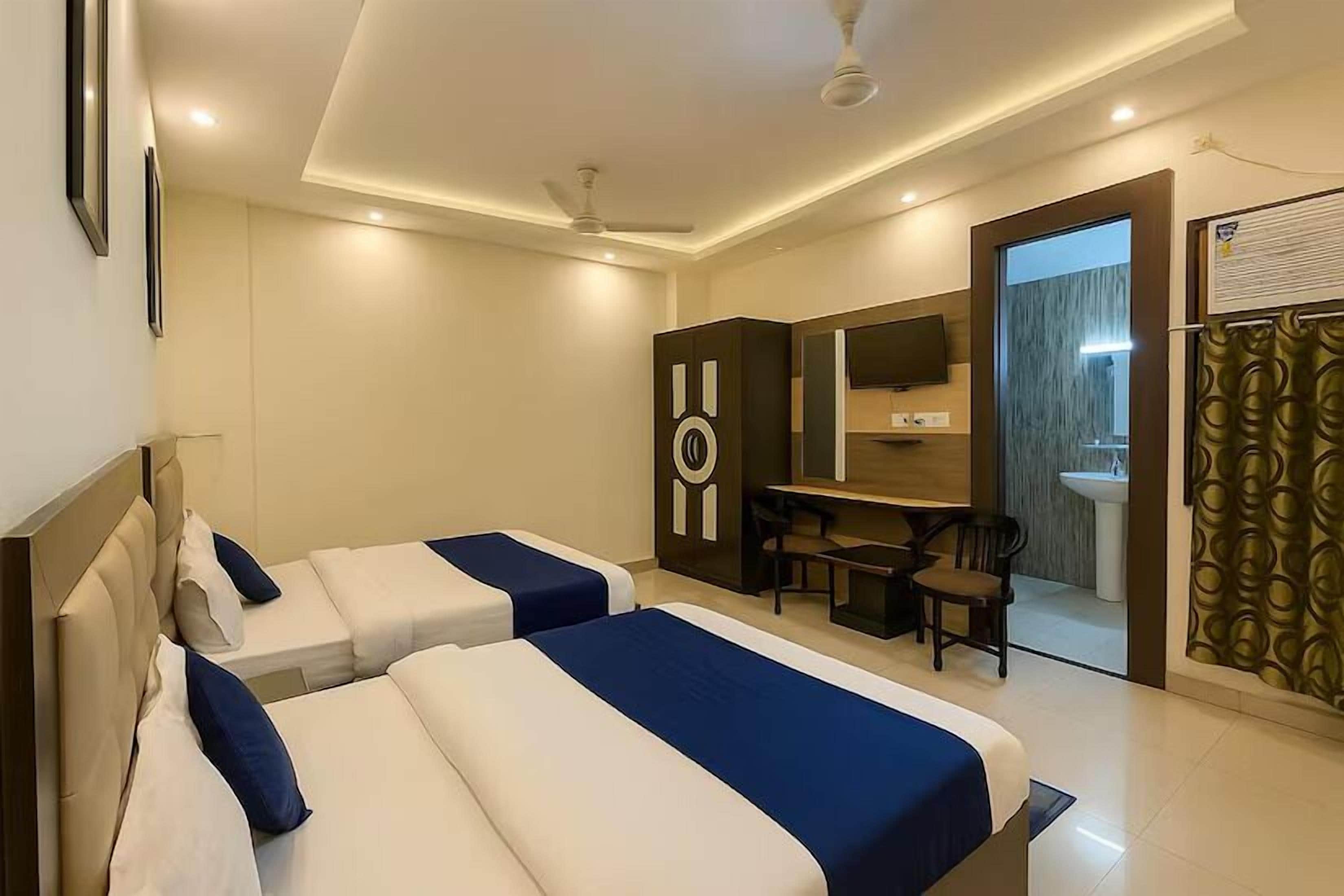 Habitación de hotel con dos camas, un escritorio, una silla, televisión y un baño a la vista a través de una puerta abierta.