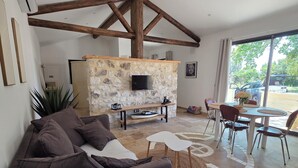 A spacious living area with a stone fireplace, a sofa, a dining table with chairs, and a large window offering a view of the outdoors. - La cabanette in the Camargue (Arles)