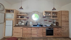 A kitchen with wooden cabinets, a built-in oven, a sink, and a window with a view of greenery. - La cabanette in the Camargue (Arles)