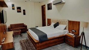 Une chambre à coucher avec un grand lit, une tête de lit en bois, des tables de chevet, un bureau, une chaise et un appareil de climatisation.