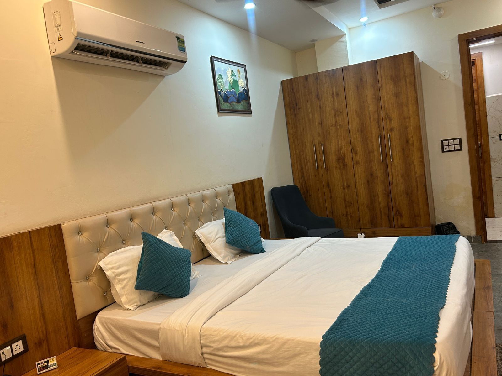 A hotel room with a bed, a wardrobe, a chair, and an air conditioning unit.