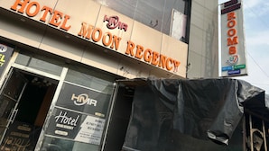 Un hôtel appelé « Hotel Moon Regency », avec une enseigne indiquant qu’il propose des équipements tels qu’une salle de réception, des chambres climatisées et un restaurant.